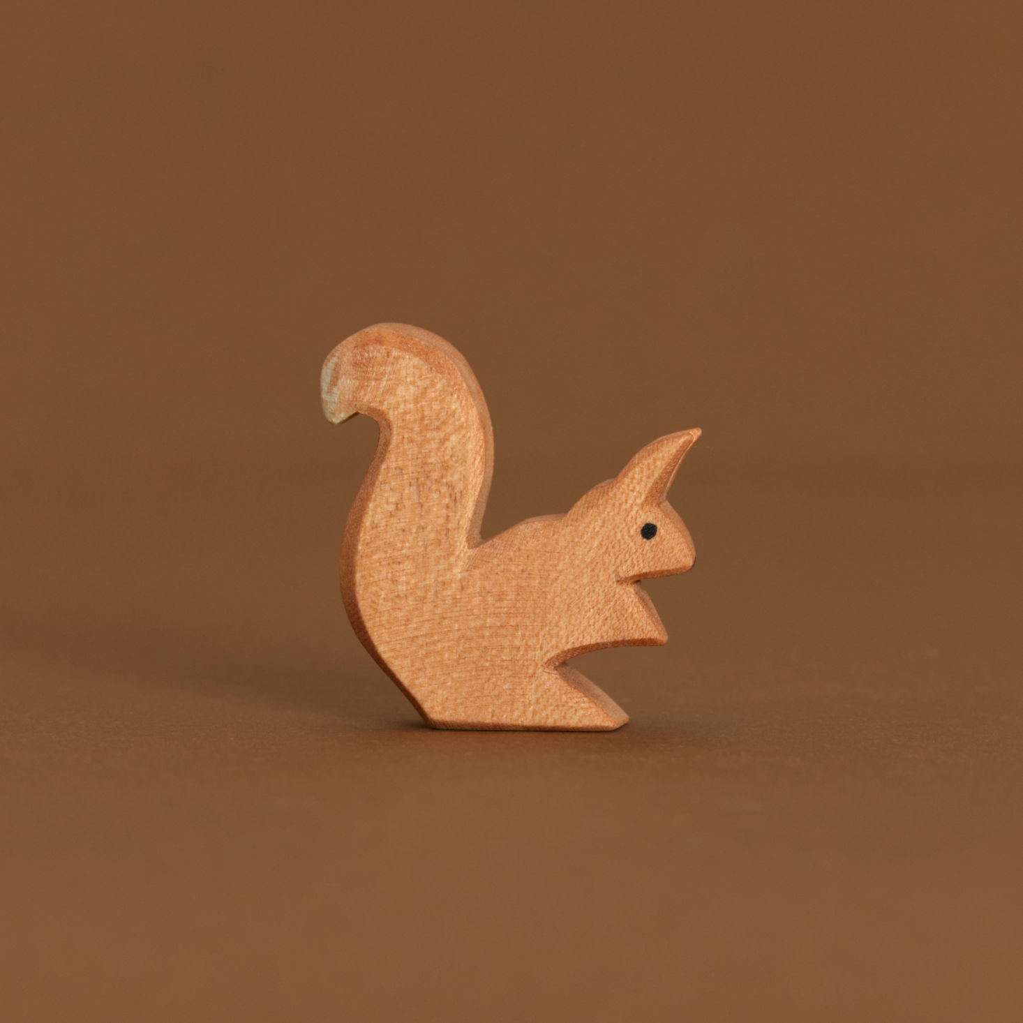 Ostheimer Eichhörnchen sitzend, aus Naturholz gefertigt. Es ist leicht nach vorne gebeugt, genauso das Ohr. Der Schwanz mit weißer Spitze zeigt jedoch nach oben.
