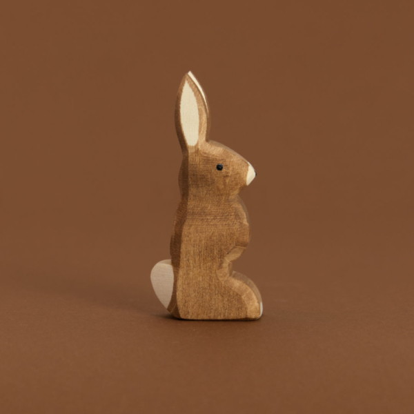 Ein brauner Hase mit nach oben zeigenden Ohren, von Ostheimer aus Naturholz gefertigt, schaut im Profil nach rechts, hat eine weiße Blume und Nasenspitze.