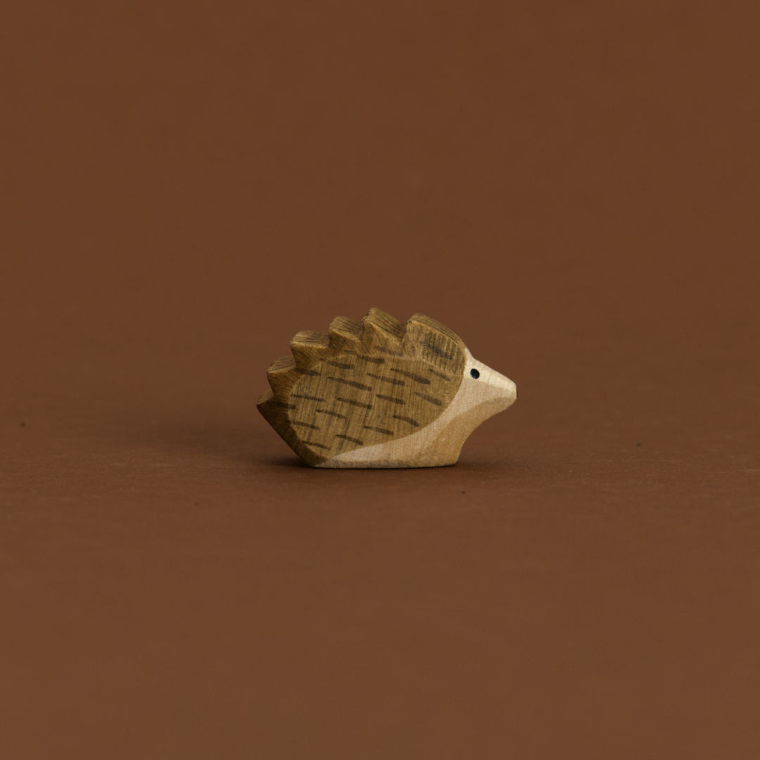 Ein kleiner Igel von Ostheimer aus Naturholz gefertigt, schaut im Profil nach rechts, hat dunkelbraune Stacheln und naturfarbenes Bauchfell.