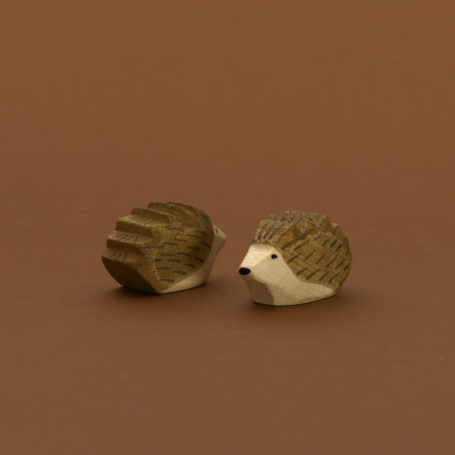 Zwei kleine Igel von Ostheimer aus Naturholz gefertigt, beide haben dunkelbraune Stacheln und naturfarbenes Bauchfell. Der Rechte schaut nach vorne links und der Linke nach hinten rechts.