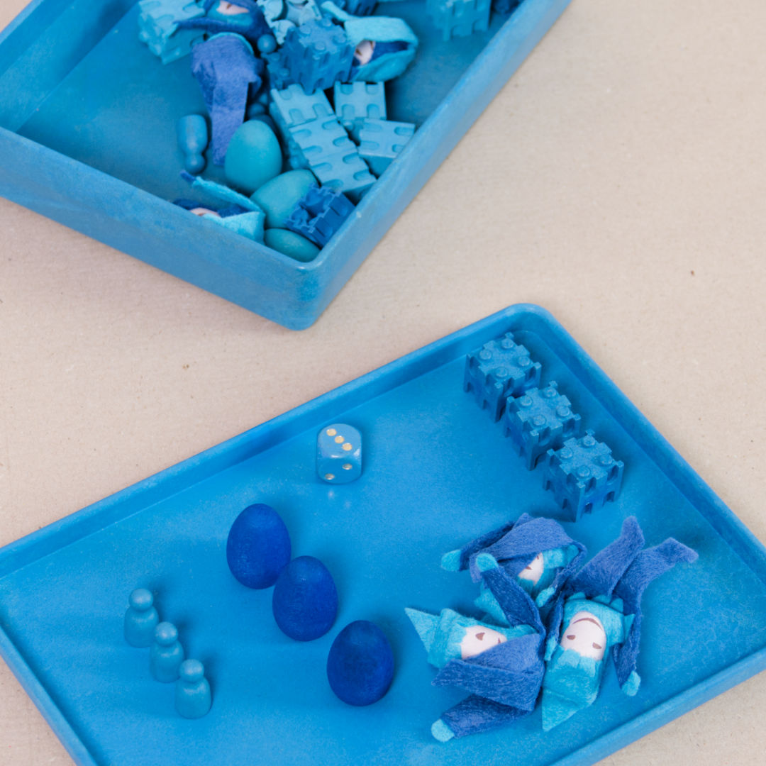 Komposition aus der aus recyclebarem Material bestehende blaue Box von Wissner mit kleinen Spielsteinen und Figuren.