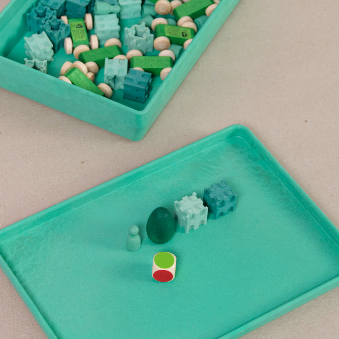 Komposition aus der aus recyclebarem Material bestehende grüne Box von Wissner mit kleinen Spielsteinen und Figuren.