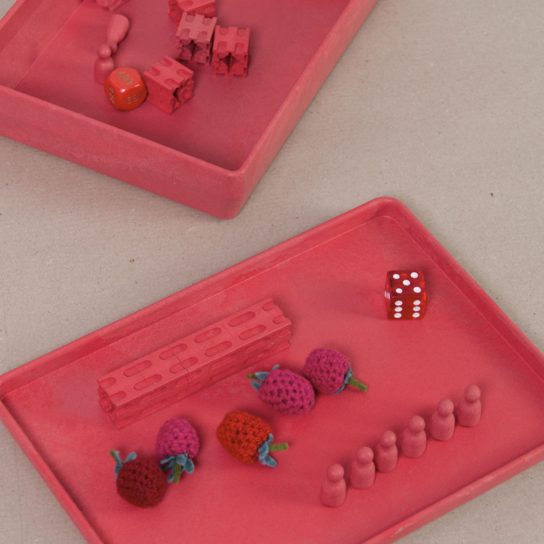 Komposition aus der aus recyclebarem Material bestehende rote Box von Wissner mit kleinen Spielsteinen und Figuren.
