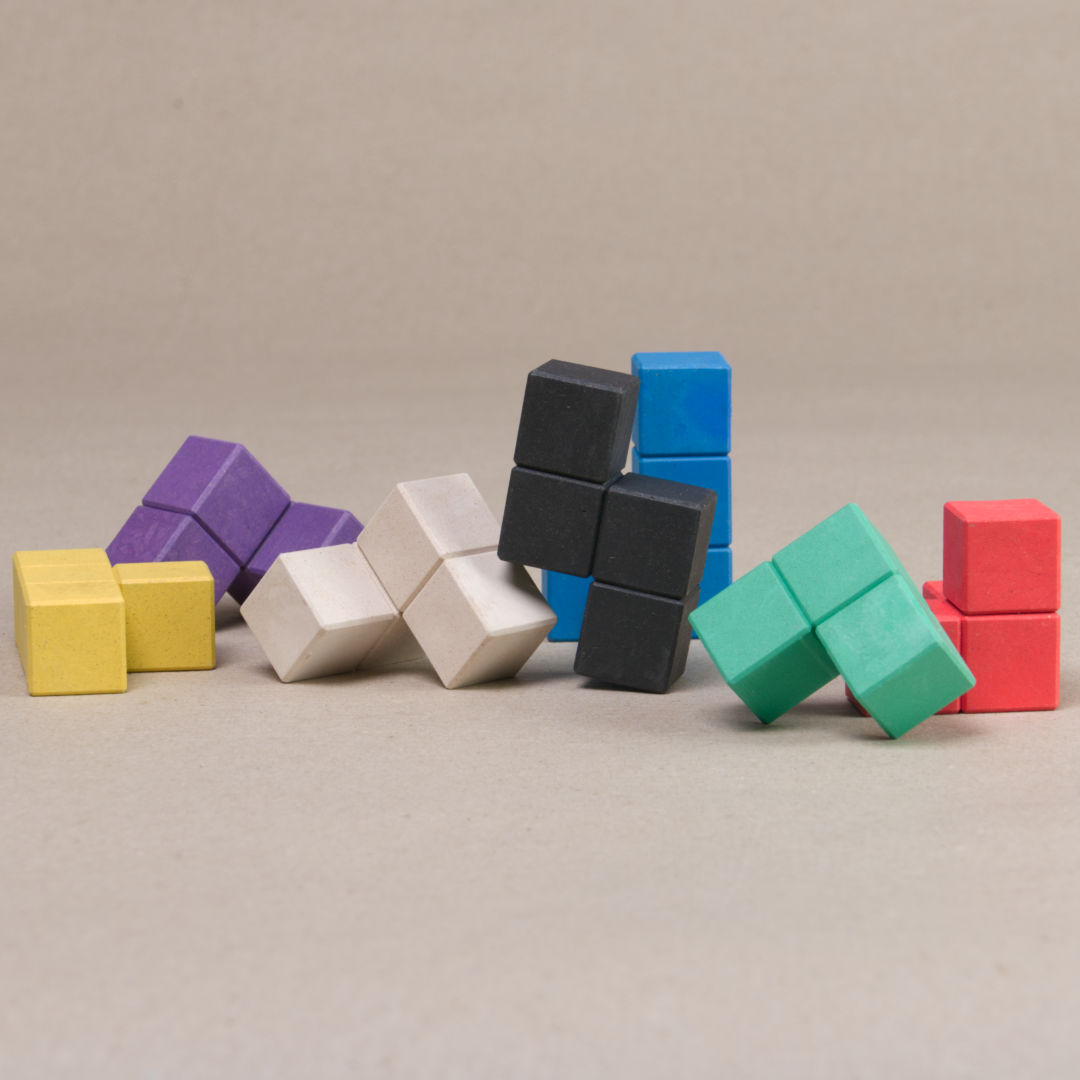 Komposition aus den verschiedenen Bausteinen des Somawürfels aus recycelbarem Material in 7 Farben. Blau, gelb schwarz, grün, lila und rot.