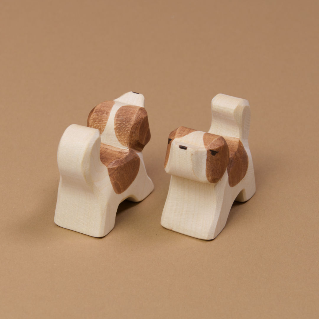 Zwei kleine Bernadiner aus Naturholz von Ostheimer gefertigt. Beide haben helles Fell mit einem braunen Fleck auf dem Rücken und braunen Ohren. Beide schauen aneinander vorbei. Der Rechte nach vorne links und der Linke nach hinten rechts.