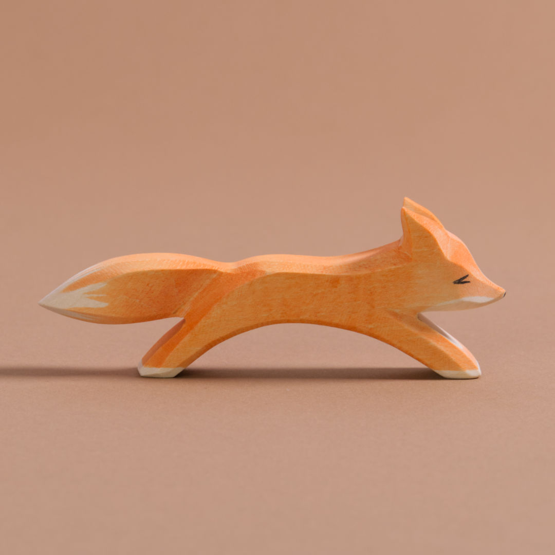 Ein grosser Fuchs ist in laufender Position, hat orangenes Fell, einen Schwanz mit weißer Spitze und weißes Bauchfell. Es schaut nach rechts.