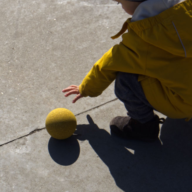 Ein Kind greift nach dem gelben Korkball aus em §er-Kugel Set C von Korxx.