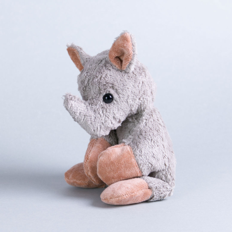 Dasitzendes Kuscheltier Nashorn Timmy mit grauem Plüschfell, schwarzen Glasaugen, sowie rosa Ohren und Hände, Horn und einem lächelnden aufgenähten Mund.
