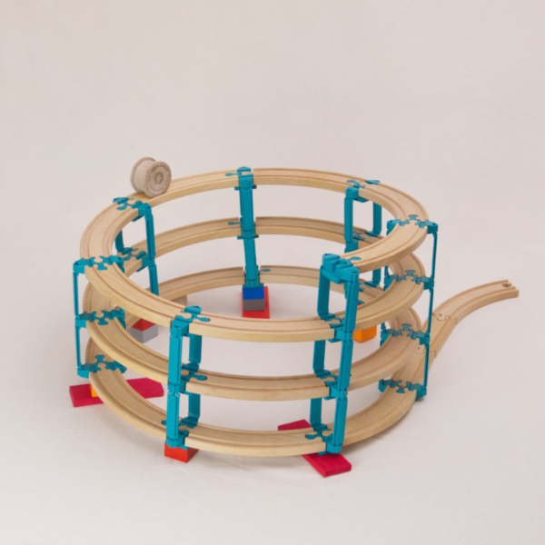 Das Adapter Set Helix 3 von Yamba ermöglicht es mit seinen Bauelementen die Verbindung von Klemmbausteinen (DUPLO®, BioBUDDi®, Hubelino® usw.) und Schienen (BRIO®, IKEA®, Eichhorn®, Hape® usw.) in ein Säulensystem auf zu bauen, was über mehrere Ebenen gehen kann. Zu sehen ist das Set Helix 3, das mittlere Paket mit insgesamt 57 Elementen, mit diesen kann man bis zu vier Stockwerke im Kreis nach oben bauen. Es gibt vier unterschiedliche Bauelemente: Verbindungsstück LinkUp, Verbindungsstück Cross, Säule Lift, Verbindungsknochen Bar. Zusätzlich enthält jedes Set eine Holzwalze genannt Rolli der auf den hölzernen Schienen selbstständig nach unten rollt.
