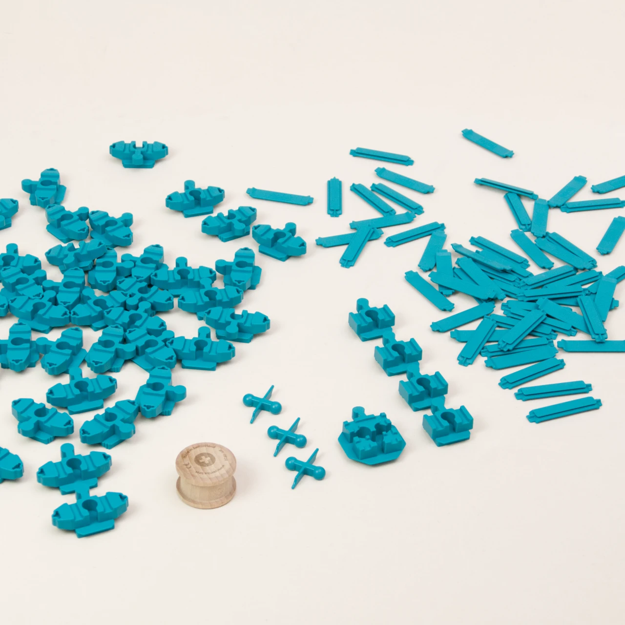 Zu sehen sind alle Elemente in dem Adapter Set Helix 5 von Yamba enthalten sind, insgesamt 104 Türkise Bausteine in fünf unterschiedlichen Formen:Verbindungsstück Link, Verbindungsstück LinkUp, Verbindungsknochen Bar, Verbindungsstück Cross, Säule Lift. Die Einzelteile sind aus hochwertigem ABS Kunststoff mit Spritzguss hergestellt. Des Weiteren enthält das Set einen Rolli, eine zylindrische Holzwalze.