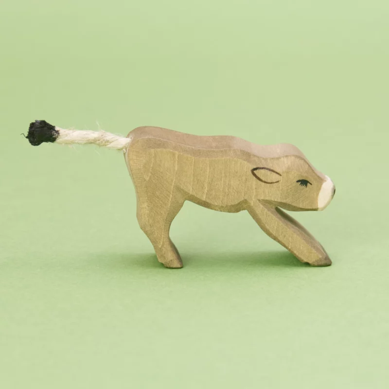 Ein Holztier Kalb der Marke Ostheimer, das nach rechts schaut. Die flach ausgesägte Figur zeigt die Silhouette eines trinkenden Kälbchens, die Kanten sind leicht abgerundet. Das Fell ist braun und die Schnauze ist weiß. Der Schwanz ist eine weiße Kordel mit schwarzer Spitze.