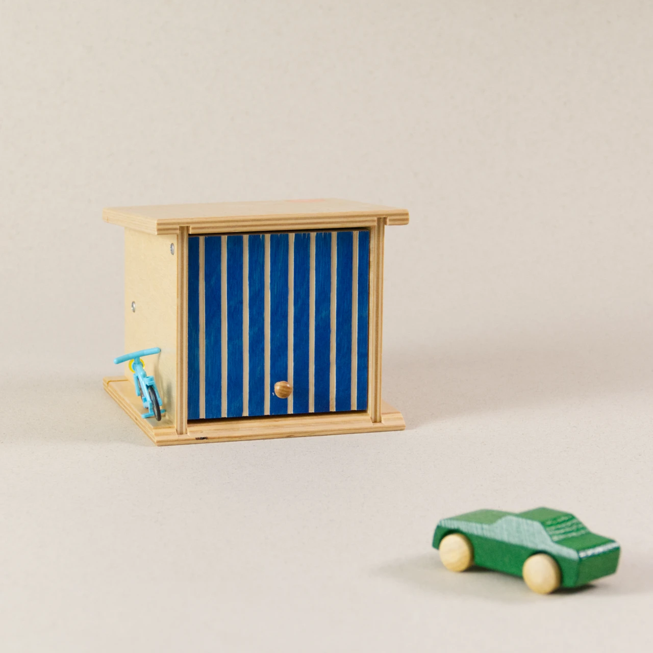Doppelgarage von Beck zum Spielen, aus Holz. Das Garagentor ist blau und lässt sich aufklappen. Ein grünes Auto aus Holz ist zusätzlich zu sehen.