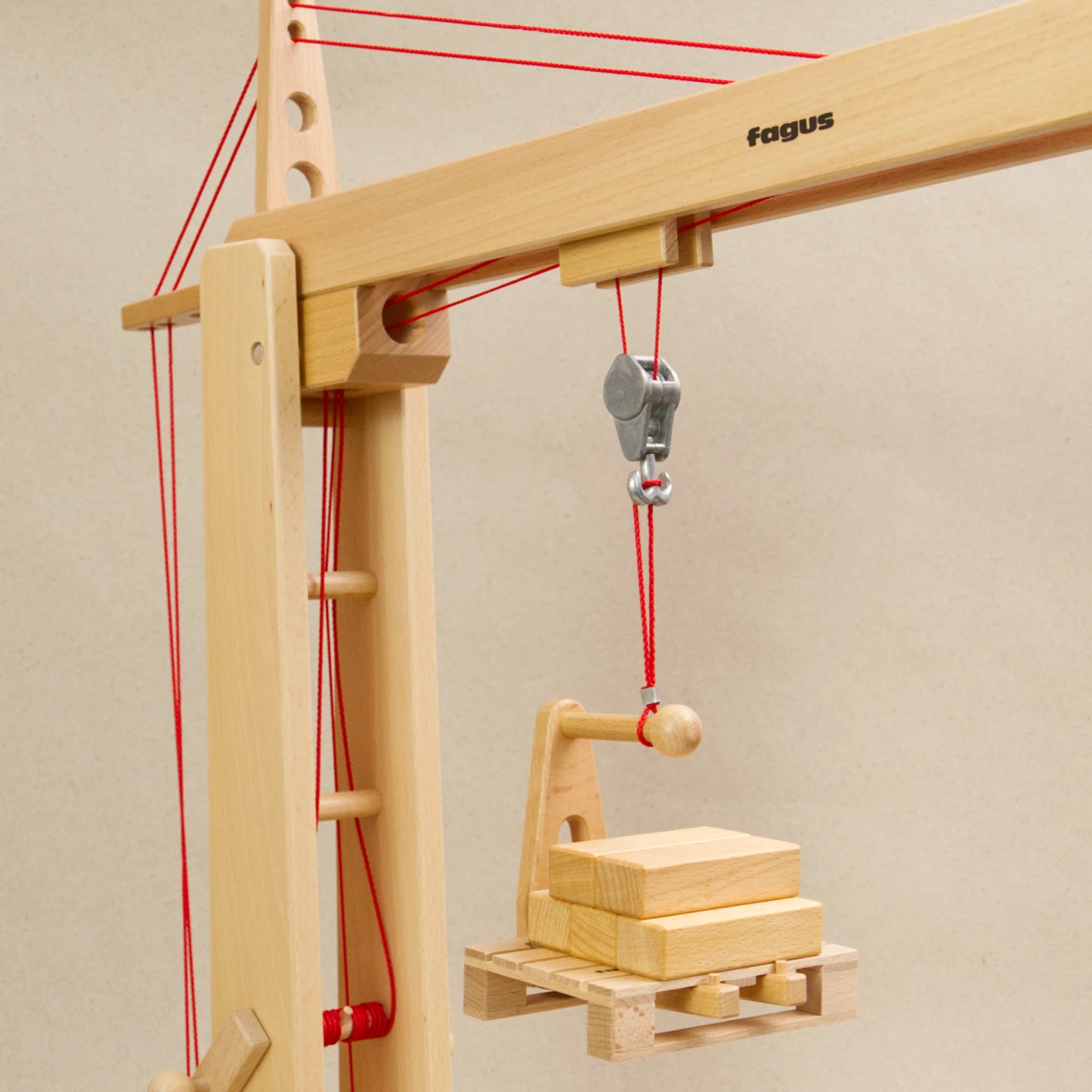 Ladegabel von fagus aus naturlackiertem Buchenholz mit roter Verbindungsschnur am Haken vom fagus Hochkran angebracht. Die Ladegabel schwebt in der Luft und ist mit einer Europalette mit Holzblöcken beladen, Nahaufnahme.
