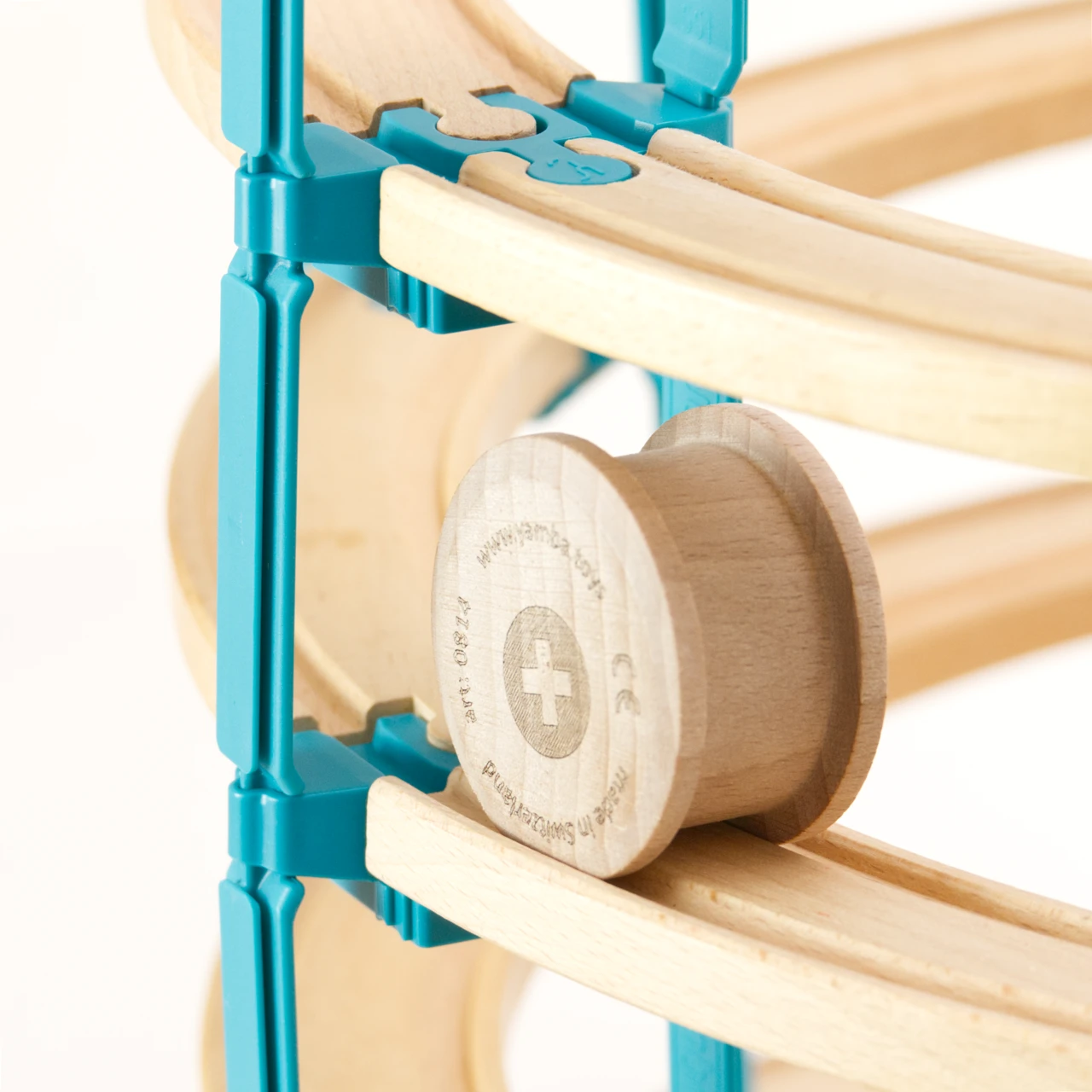 Zu sehen ist eine Rolli Holzwalze von der Marke Yamba auf einer mehrstöckigen Spielzeug Holzschienebahn. Die Schienen sind mit den Verbindungselementen LinkUp und Lift aus dem Helix Set von Yamba zusammengebaut. Der Rolli hat die Form eines Zylinders, der an den Enden jeweils etwas Überstand hat, um in der Schienen selbst nach unten rollen zu können. Der Rolli ist aus naturbelassenem Buchenholz.