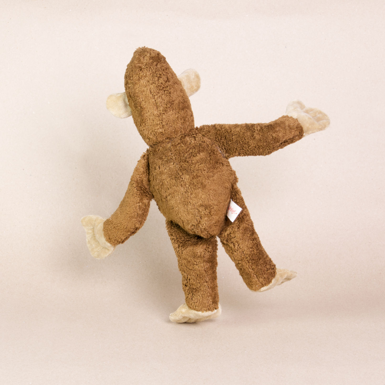 Hinteransicht des Kuscheltieres Affe namens Toto von Kallisto. Es hat braunes Plüschfell und braune Knopfaugen. Sein Körper ist leicht nach links geneigt und steht nur auf dem linken Bein.
