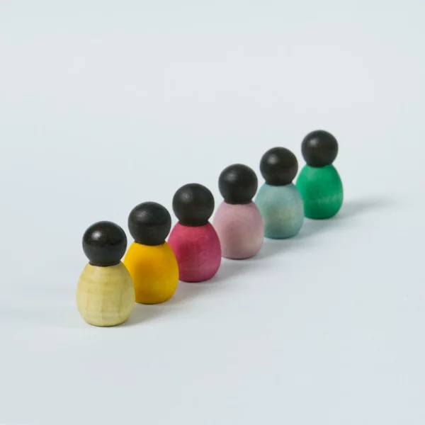 sechs kleine Babyholzfigurenmit dunkler Hautfarbe und verschiedenen Körperfarben in eine Reihe aufgestellt.