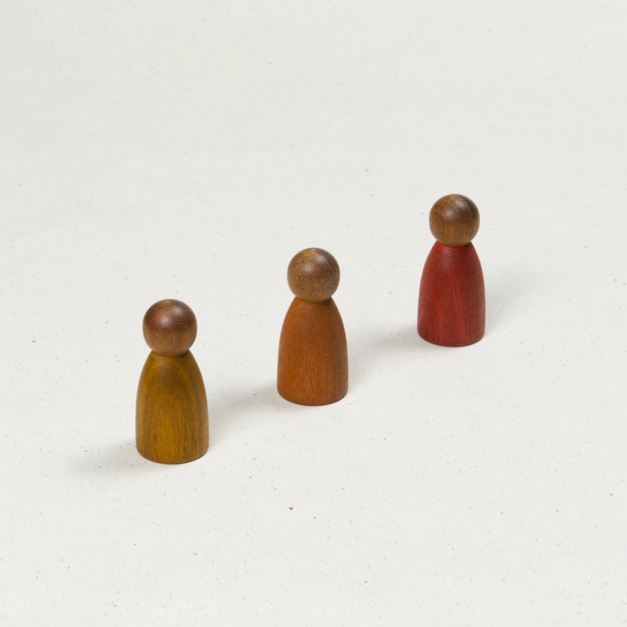 Drei gleichförmige Holzfiguren mit dunklerer Hautfarbe und Körpern in Gelb, Orange und Rot.