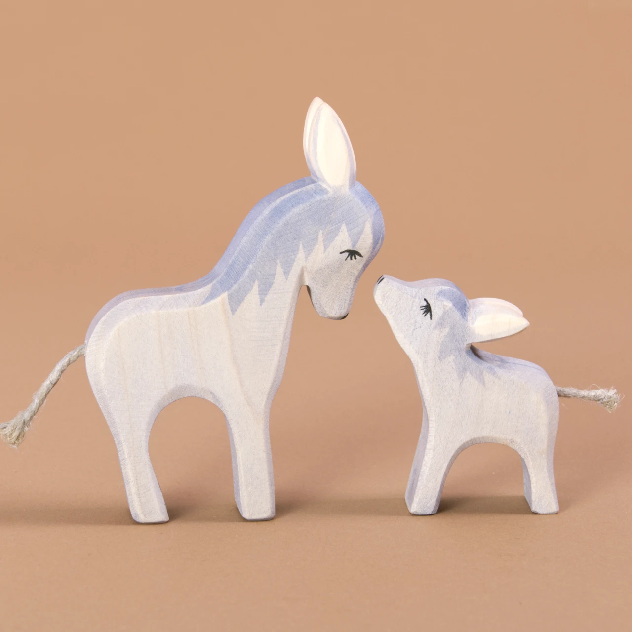 Komposition aus Esel klein und Esel gross. Beide schauen sich gegenseitig an. Der grosse zum kleinen herab und der kleine zum Grossen hinauf. Beide sind im Profil zu sehen.