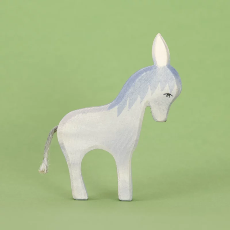 Ein stehender Esel von Ostheimer aus Naturholz gefertigt, hat hellblaues Fell und etwas dunklere Mähne, weiße nach oben hin stehende Ohren, schwarze Farbdetails und einen Schwanz aus Kordel. Es schaut im Profil mit gesenktem Kopf nach rechts.