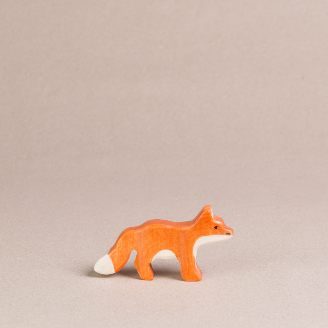 Ein nach rechts schauender, kleiner Fuchs von Holztiger, ist orange und hat eine weiße Schwanzspitze und weißes Bauchfell. Die Ohren stehen gerade nach oben.