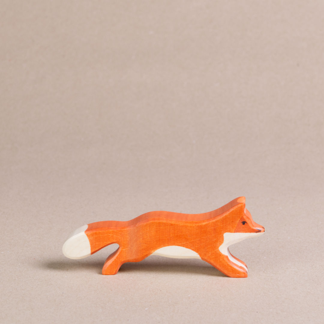 Ein nach rechts schauender, grosser, laufender Fuchs von Holztiger, ist orange und hat eine weiße Schwanzspitze und weißes Bauchfell. Die Ohren stehen gerade nach oben.