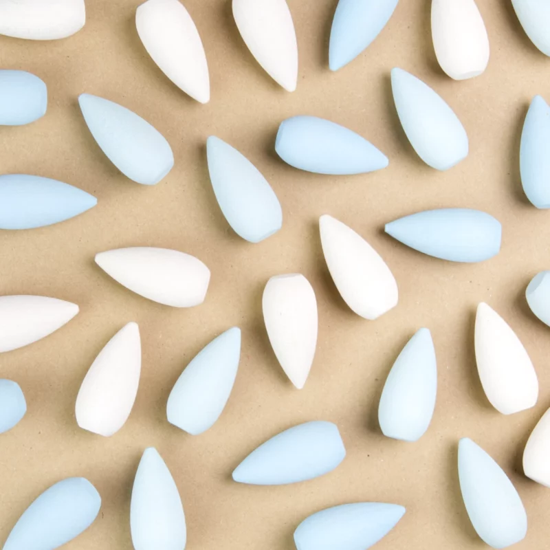 Es sind verschiedene durcheinander angeordnet tropfenförmige Holzfiguren von Grapat im Anschnitt mit weniger Abstand zueinander zu sehen. Es sind weiße, hellblaue und auch dunkelblaue Holzfiguren zu sehen.