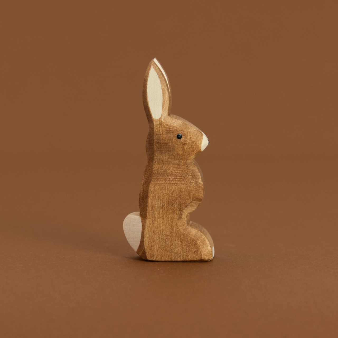 Ein brauner Hase mit nach oben zeigenden Ohren, von Ostheimer aus Naturholz gefertigt, schaut im Profil nach rechts, hat eine weiße Blume und Nasenspitze.