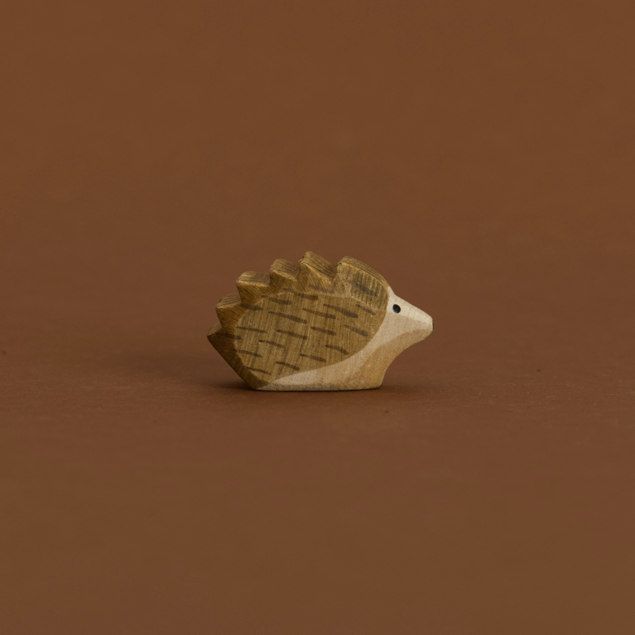 Ein kleiner Igel von Ostheimer aus Naturholz gefertigt, schaut im Profil nach rechts, hat dunkelbraune Stacheln und naturfarbenes Bauchfell.