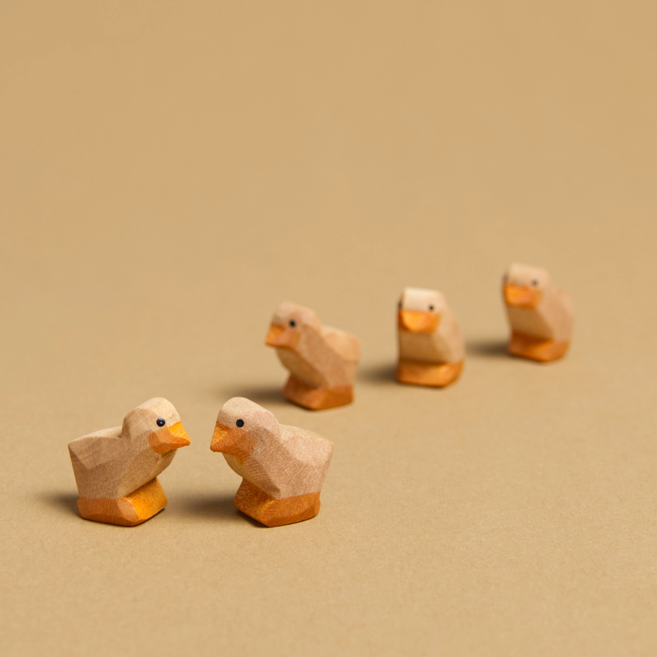 Komposition aus fünf dunklen Küken aus Naturholz von Ostheimer. Im Vordergrund schauen sich 2 gegenseitig an und im Hintergrund reihen sich 3 Küken hintereinander zum rechten Bildrand hin. Alle haben braunes Fell, orangene Schnäbel und Füße.