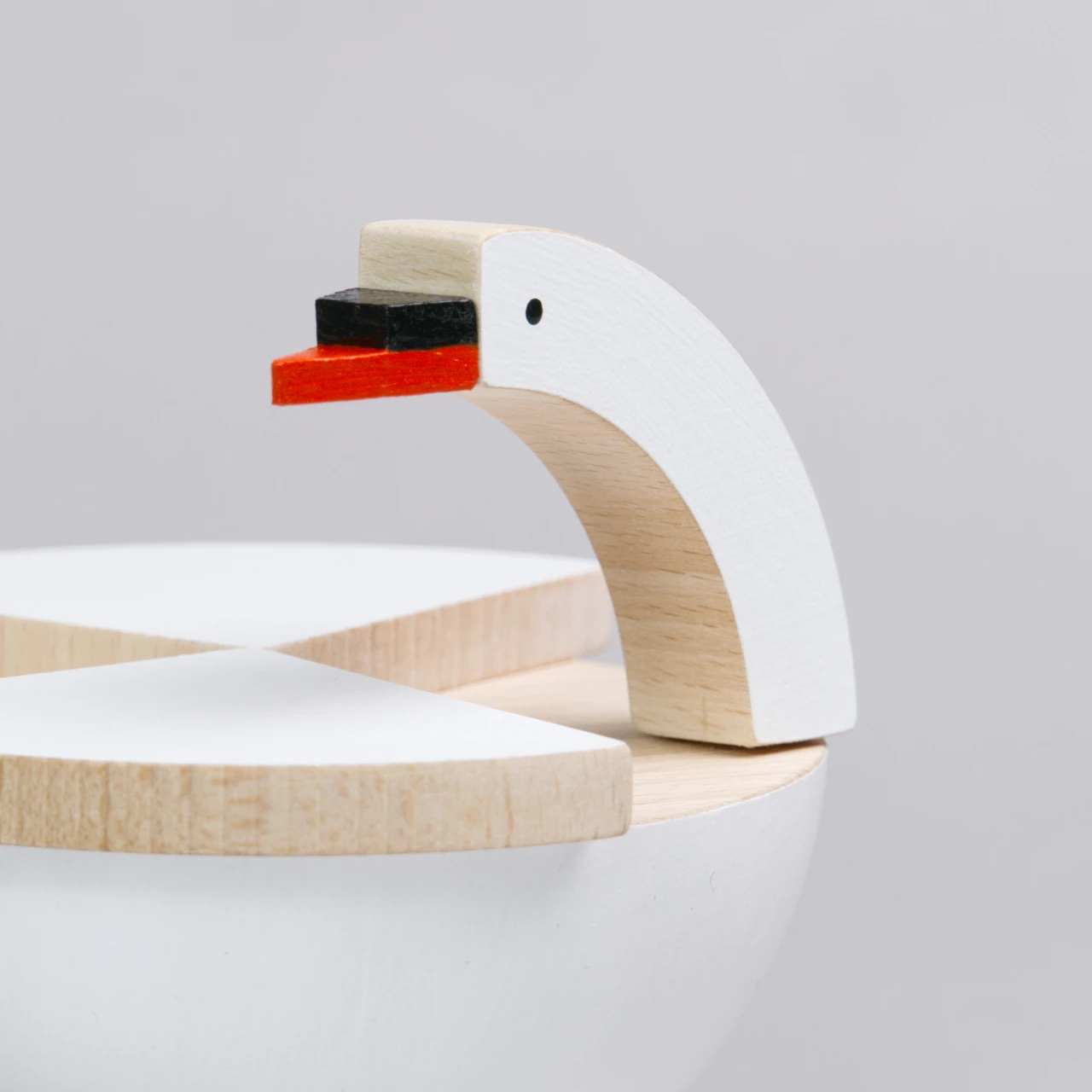 Es ist eine Nahaufnahme eines beweglichen, weißen Schwans von der Marke Kutulu zu sehen. Der Vogel ist im Anschnitt dargestellt und vorallem sein langer, runder Kopf ist im Fokus, welcher weiß bemalt ist, genauso wie die Flügel. Die äußeren Kanten sind jedoch nicht bemalt. Der Schnabel ist rot bemalt und hat eine schwarze Erhebung darauf. Der Bauch unten ist ebenfalls weiß eingefärbt.