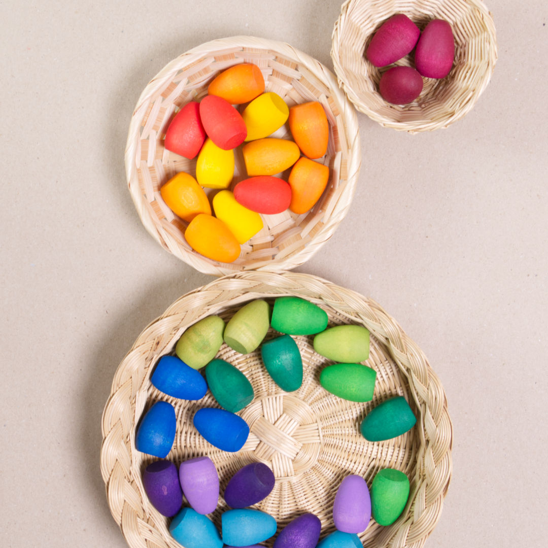Komposition aus den Figuren aus dem Set Mandala Rainbow eggs von Grapat. Alle Holzfiguren sind bunt. Alle sind in vier Körbchen aufgeteilt.