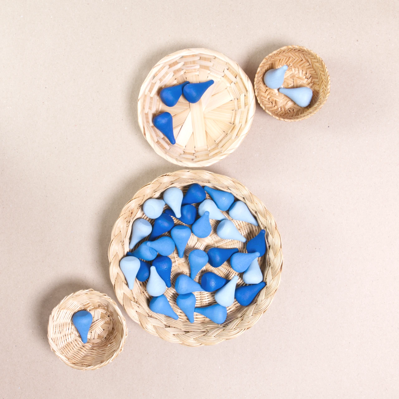 Komposition aus den Figuren aus dem Set Mandala Raindrop von Grapat. Alle Holzfiguren sind in drei unterschiedlichen Blautönen gehalten. Alle sind in vier Körbchen aufgeteilt.