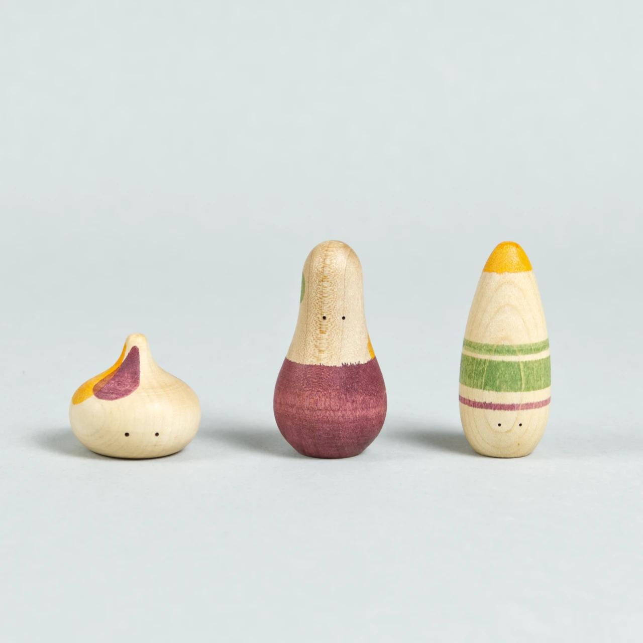Drei organisch-geformte Holzfiguren mit Augen und weinrot, grün und orangenen Bemalungen.