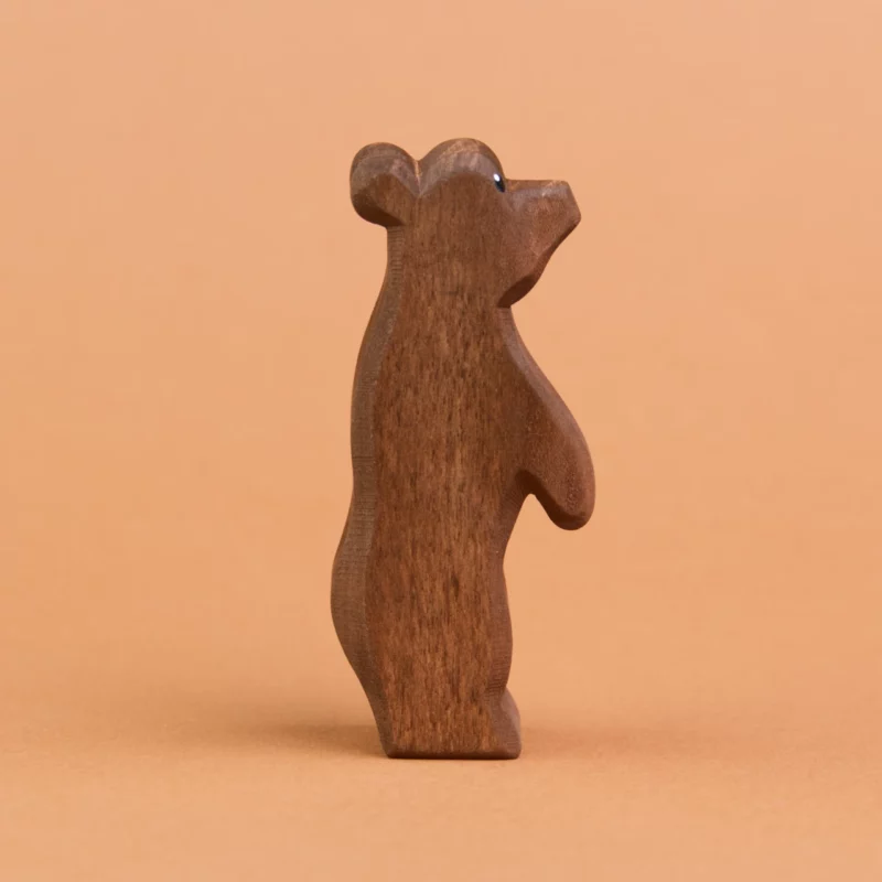 Ein kleiner Bär aus Holz ist stehend in der Seitenansicht zu sehen und schaut nach rechts, oben. Er hat dunkelbraunes Fell und große, runde Ohren. Er ist von der Marke Ostheimer.