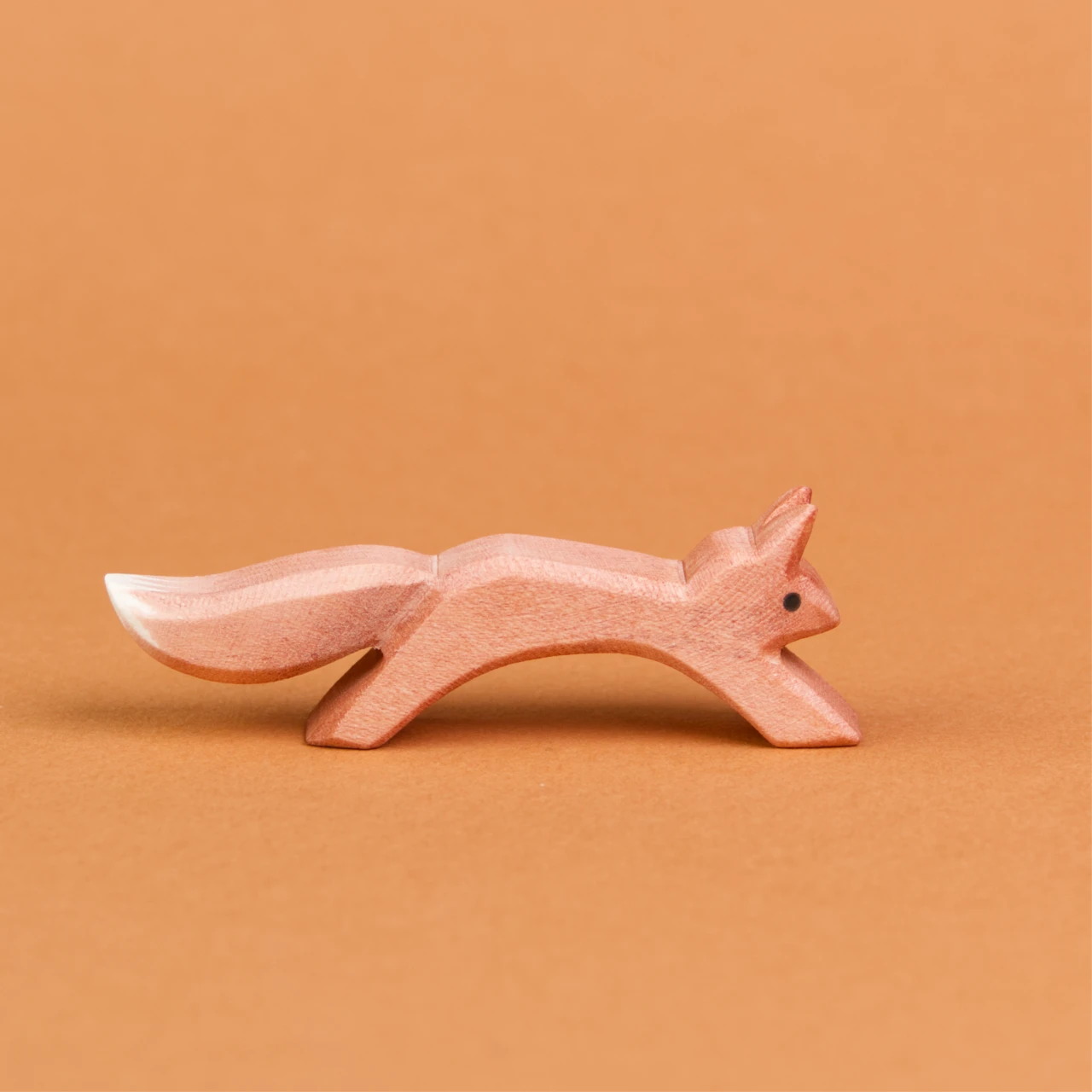 Es ist ein springendes Eichhörnchen aus Holz in der Seitenansicht zu sehen, welches nach rechts schaut. Es hat ein rötlich, braunes Fell, welches am Ende seines Schwanzes weiß gefärbt ist. Seine Ohren stehen nach oben und es ist von der Marke Ostheimer.