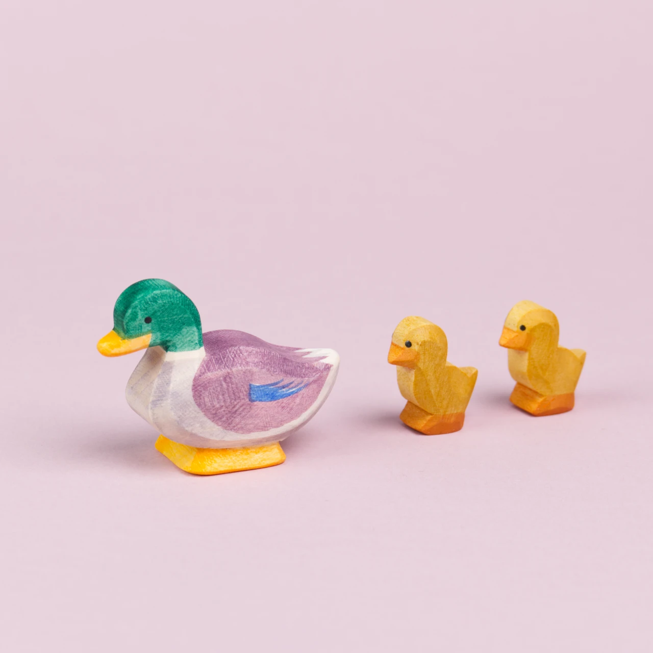 Ein Erpel aus Holz ist von der Seite mit dem Kopf nach vorne links gerichtet zu sehen. Rechts hinter ihm laufen zwei Entenküken hintereinander dem Erpel hinterher.