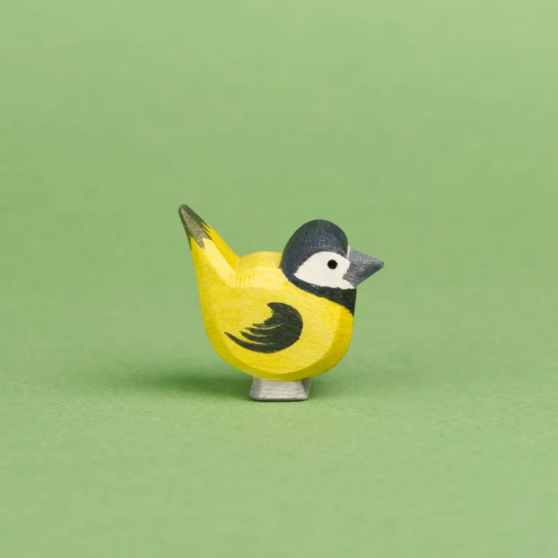 Meise aus Holz, die nach rechts schaut von der Seite zu sehen. Ihre Federn sind gelb, der Kopf, sowie die Flügel und Schwanzfedern sind schwarz. Das Gesicht ist weiß bemalt und der Schnabel grau, von der Marke Ostheimer.