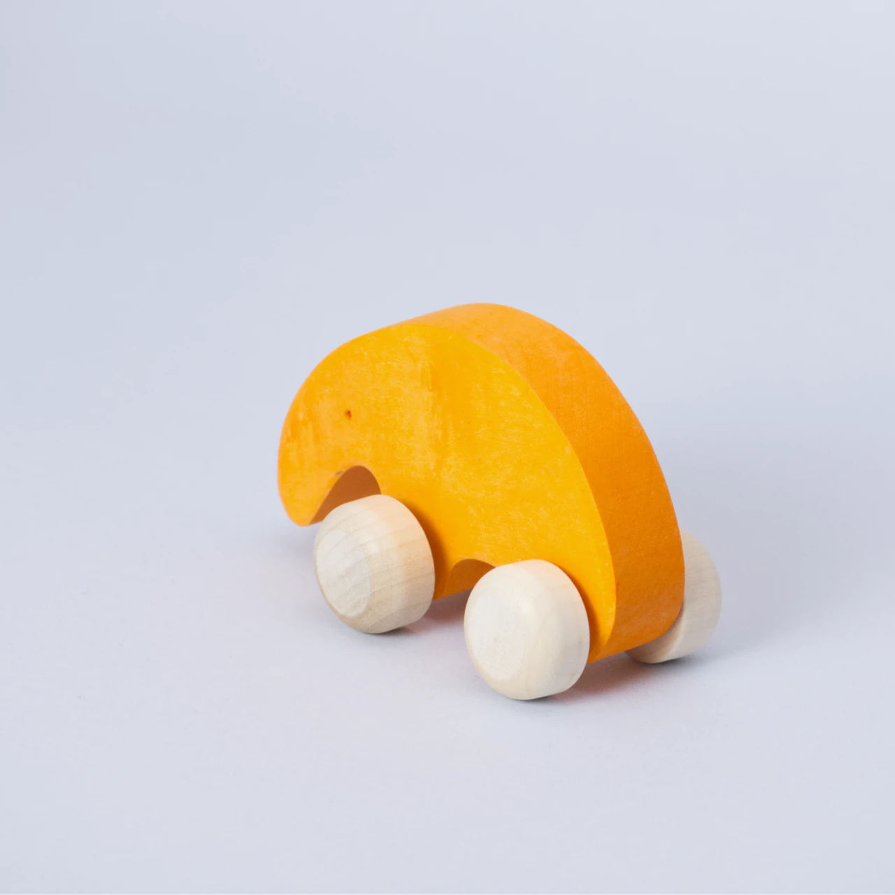 Ein orangenes Schiebetier mit weißen Rollen von Goki Evolution ist schräg von hinten zu sehen. Die Form erinnert an einen Ameisenbär mit seiner langen Schnauze. Das Spielzeugtier schaut nach hinten links mit einem kleinen Loch als Auge. Es ist aus Holz gefertigt und die Farbe ist ein warmes Orange.