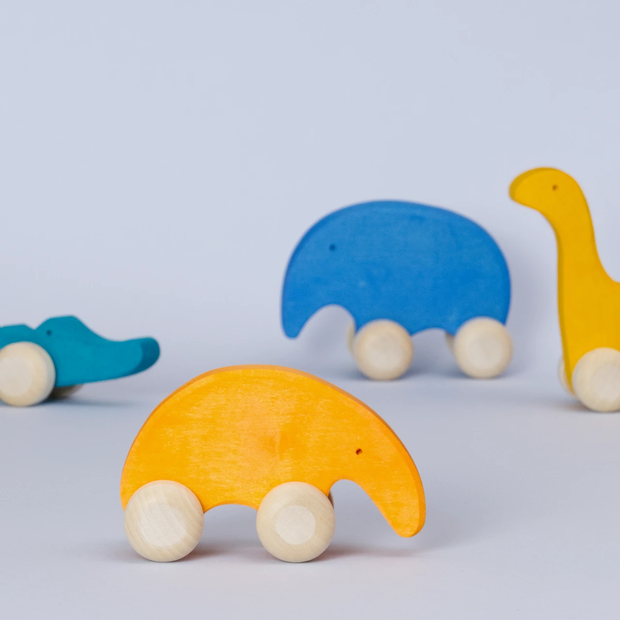 Ein Gruppenbild von den Holz Schiebetieren von Goki Evolution. Der orangene Ameisenbär steht im Vordergrund und schaut nach rechts. Das grüne Krokodil, der blaue Elefant und der gelbe Dinosaurier sind unscharf im Hintergrund.