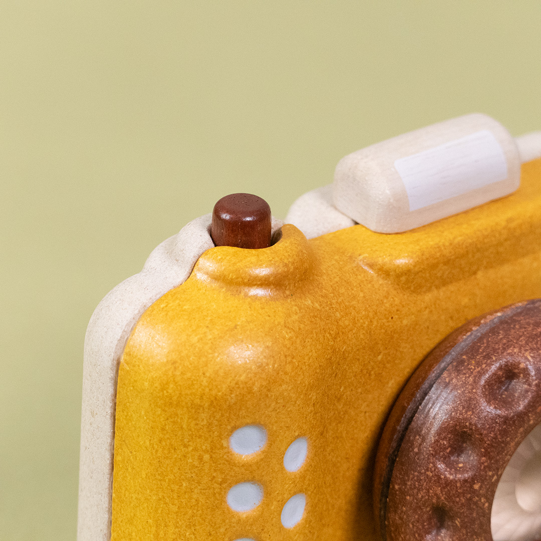 Detailaufnahme der Kamera Orchard in senfgelb, braun und naturfarben von Plan Toys. Zu sehen ist der Auslöseknopf und Blitz.