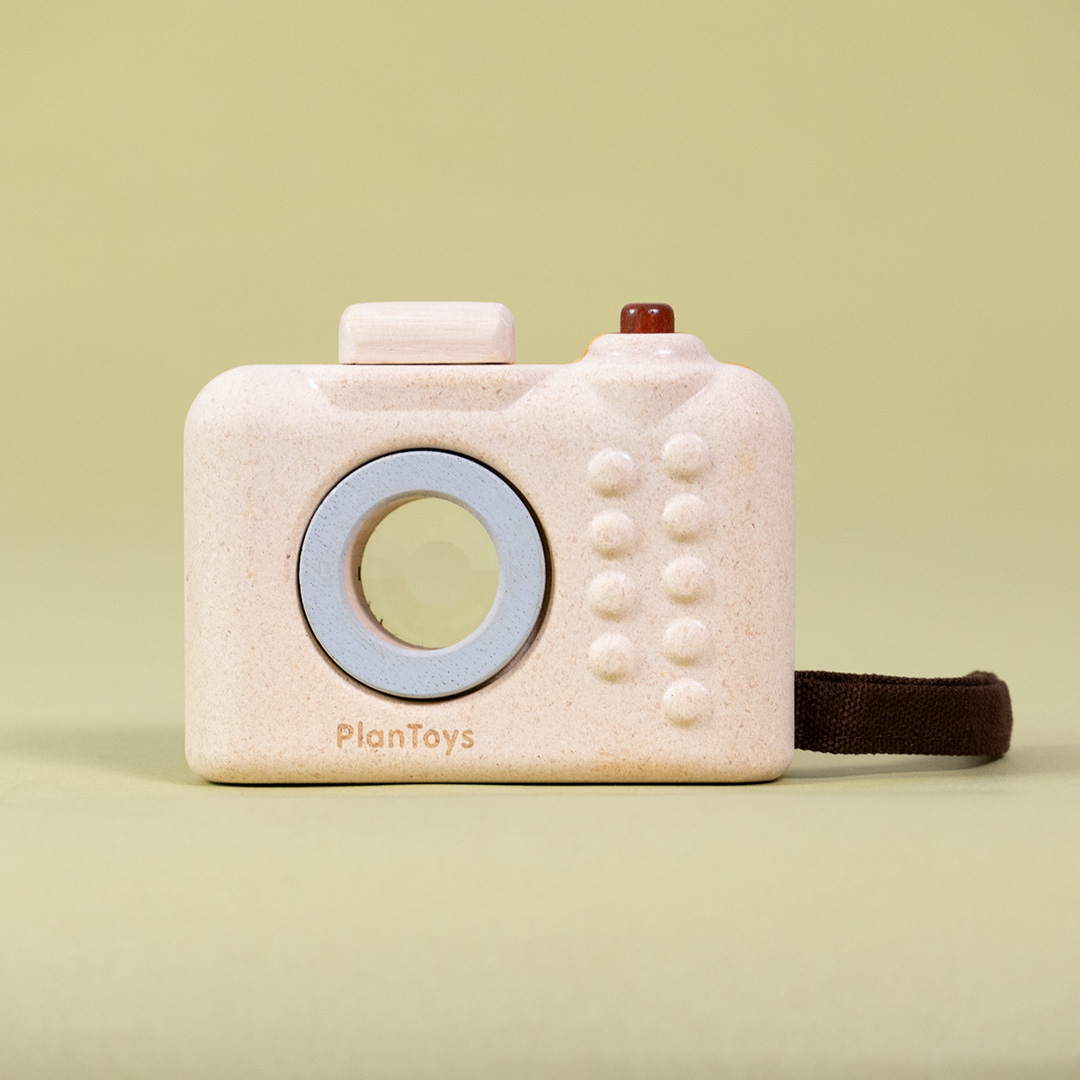 Rückansicht der Kamera Orchard von Plan Toys mit einer braunen Stoffschlaufe, bedienbarem Auslöseknopf und Blitzaufsatz.
