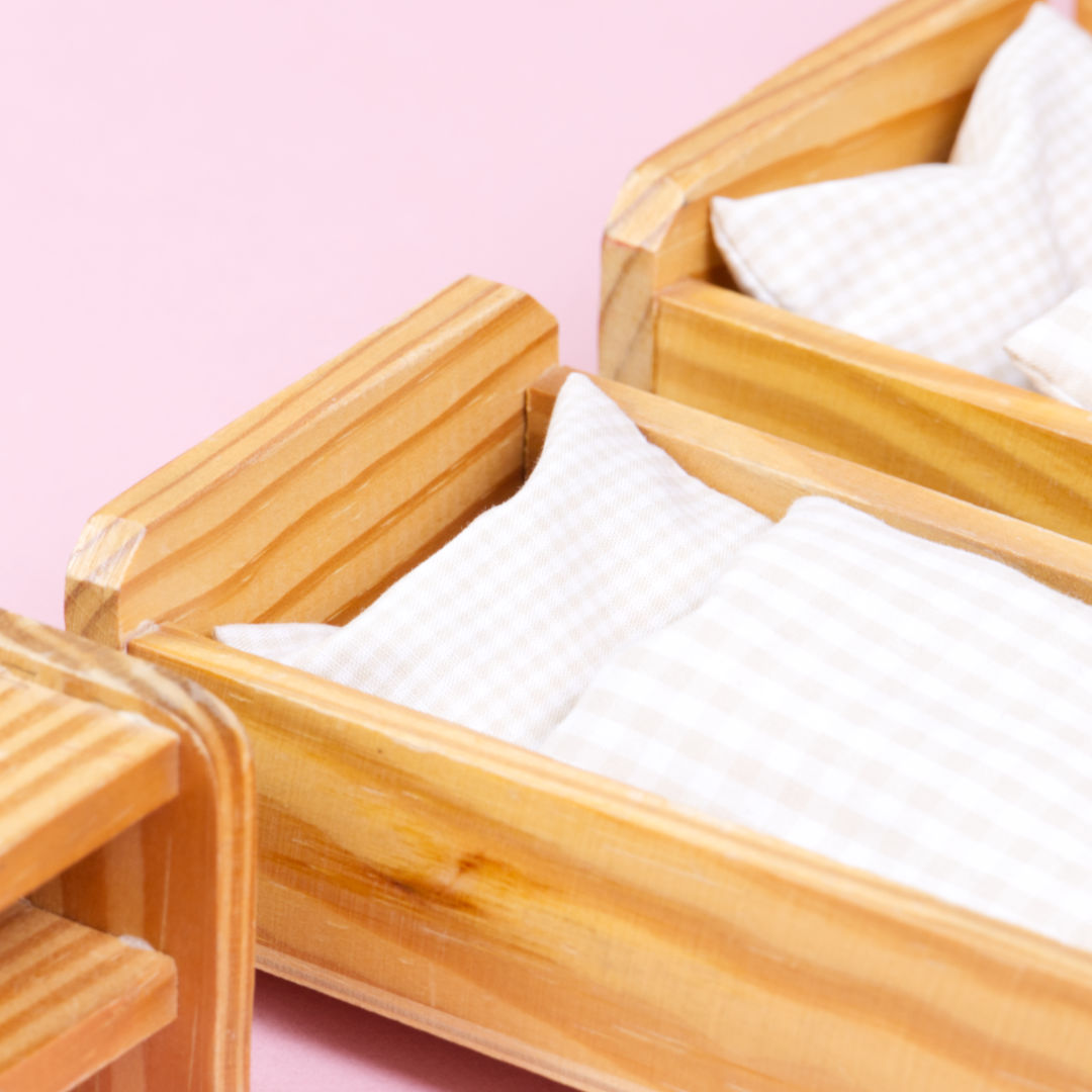 Nahaufnahme von zwei nebeneinander stehenden Holzbetten mit jeweils einem Beistelltisch und Bettwäsche mit hellbeige Karomuster.