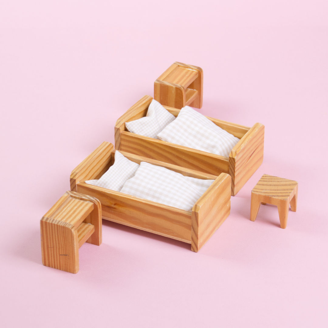Zwei nebeneinander stehende Holzbetten mit jeweils einem Beistelltisch und Bettwäsche mit hellbeige Karomuster und einem Hocker.