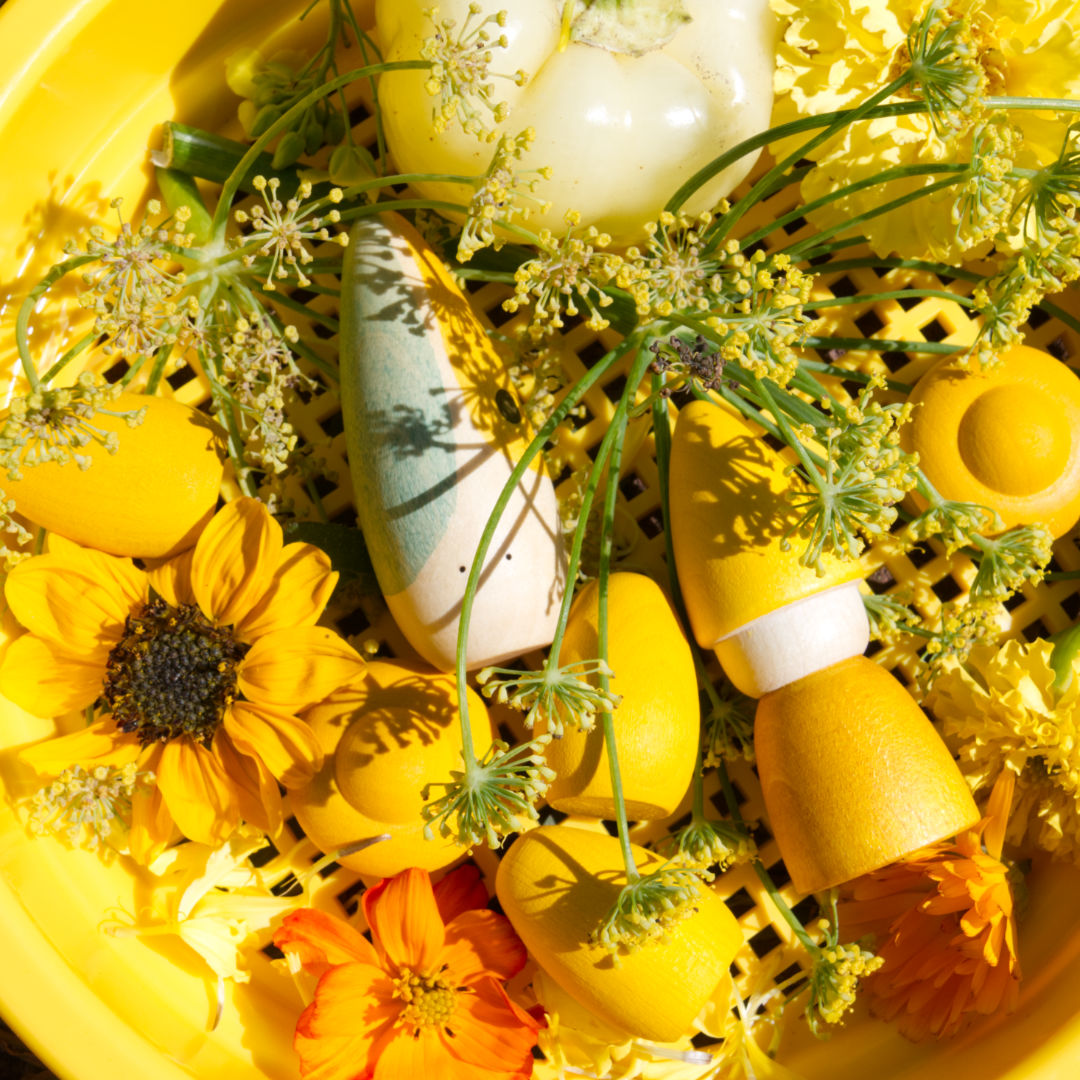 Nahaufnahme von sieben Figuren der Firma Grapat daliegend auf dem gelben Sieb von Spielstabil in Kombination mit unterschiedlichen Blumen und Naturprodukten.