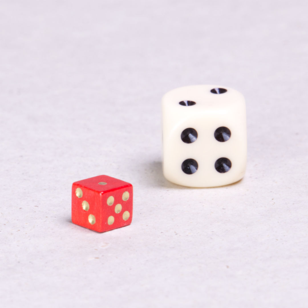 Ein roter kleiner Spielwürfel mit goldenen Punkten. Daneben zum Vergleich ein Spielwürfel in Normalgröße.