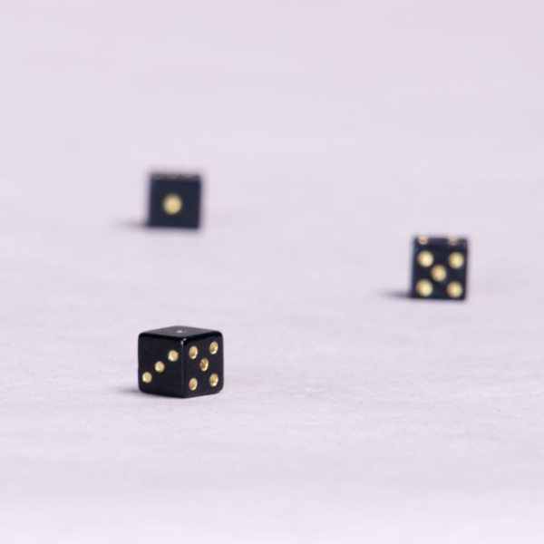 Drei schwarze kleine Spielwürfel mit goldenen Punkten.