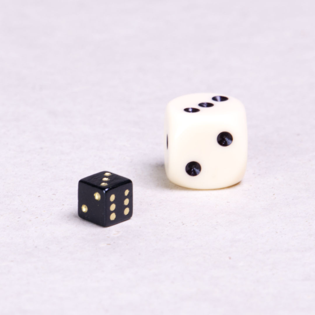 Ein schwarzer kleiner Spielwürfel mit goldenen Punkten. Daneben zum Vergleich ein Spielwürfel in Normalgröße.
