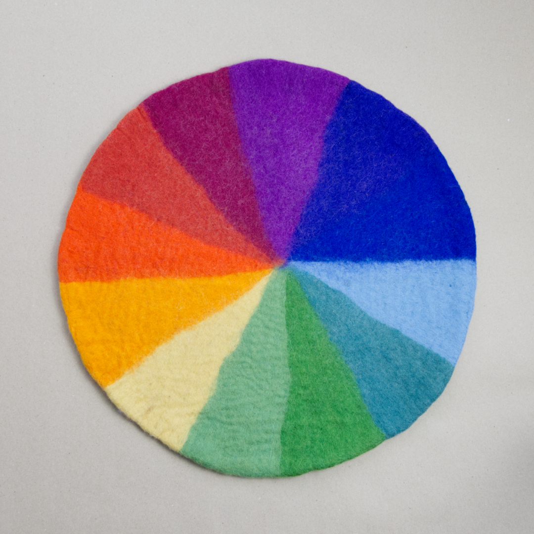 Es ist ein Farbenkreis aus Filz von der Marke Bauspiel zu sehen. Die Farbfelder darauf sind nach dem Schema eines Regenbogens angeordnet. Des Farbfeld ist in Form eines spitzen Dreiecks dargestellt.