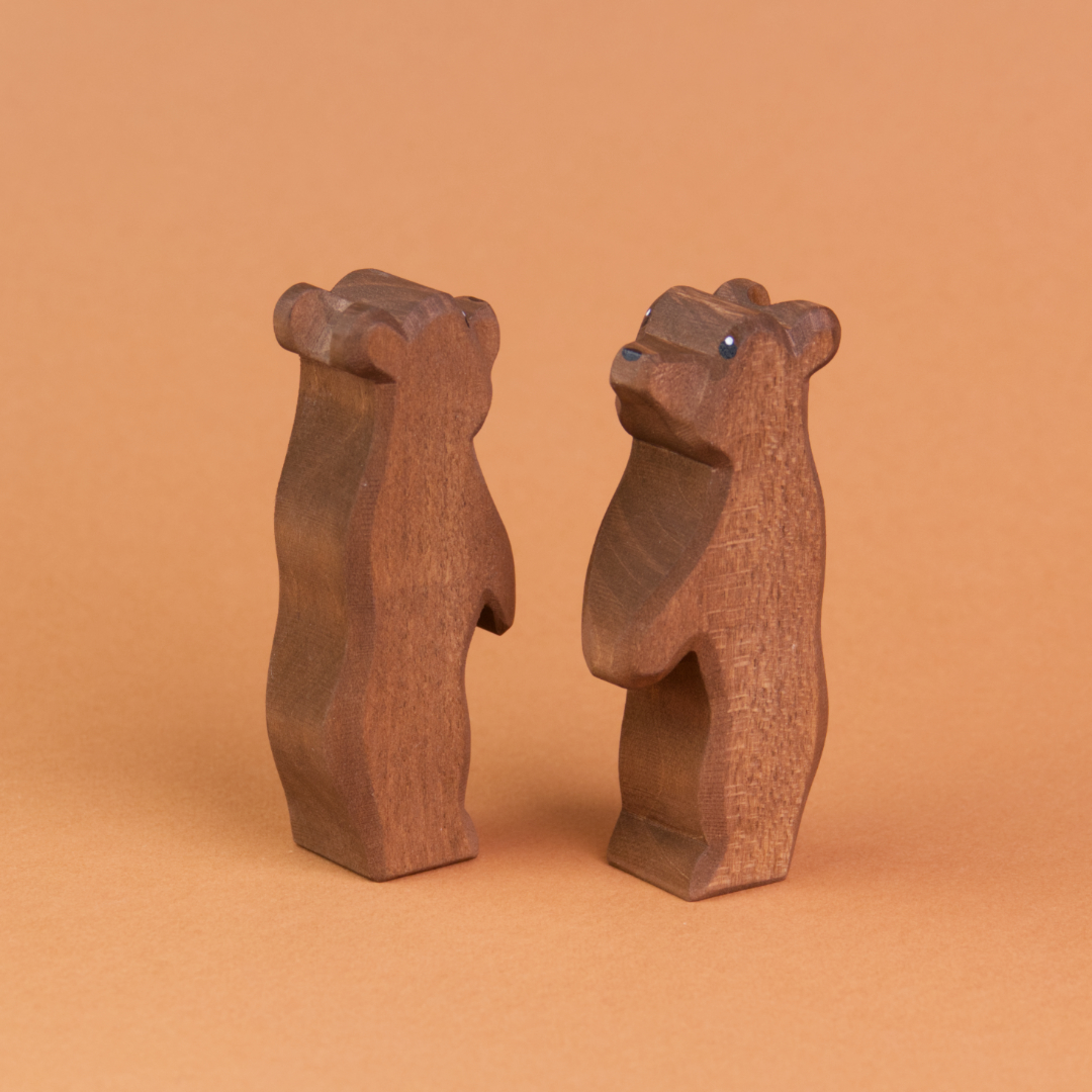 Zwei kleine Bären aus Holz sind schräg nebeneinander stehend zu sehen. Der recht Bär schaut nach vorne links hoch, der linke Bär schaut nach hinten rechts nach oben.