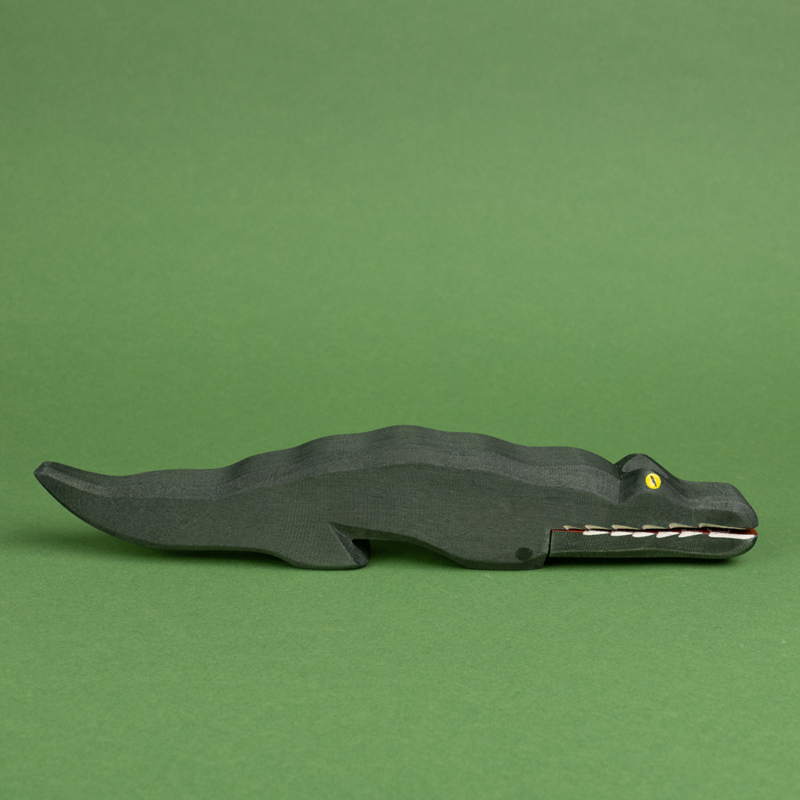 Ein dunkelgrünes Krokodil aus Holz ist in der Seitenansicht zu sehen. Es hat gelbe Augen und weiße, lange Zähne und ist von der Marke Ostheimer.